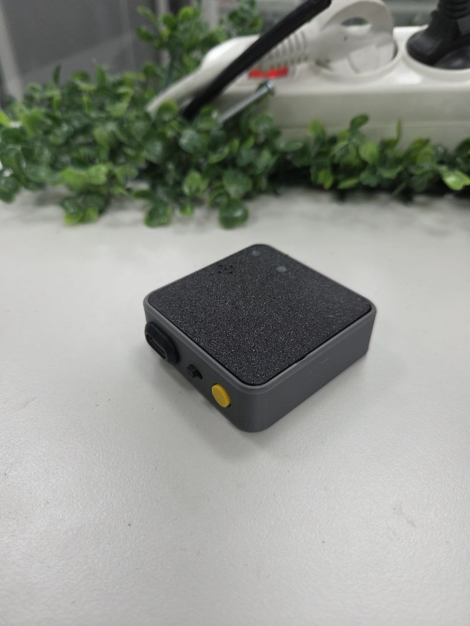 회색 정사각형 케이스와 검은 상단 패널, 측면 USB-C 포트와 노란색 버튼이 보이는 AI Meeting Recorder 실물 시제품